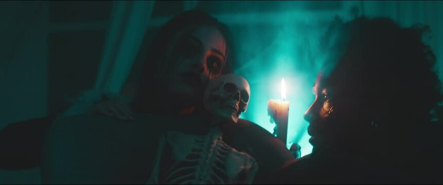 Two attractive scary vampires crowl over a skeleton with a blue light and smoke, holding a candlelight