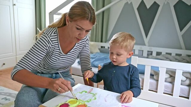 Cute little boy and mother painting together at home