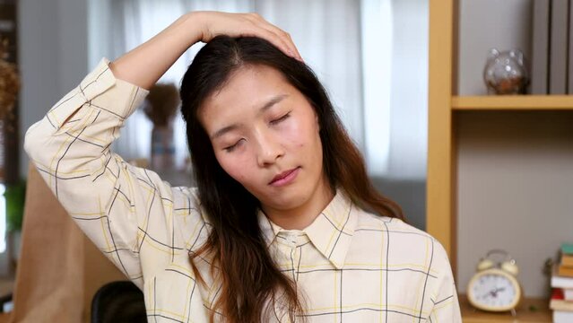 Young tired Asian ethnicity woman stretching neck and shoulder after working at home office desk long period sitting, female freelancer closed eye exercise relax rest muscle from long time at work