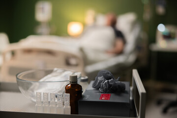 Medication stand in focus, while a man rests in the hospital, slightly blurred in the background