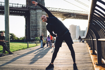Flexible man doing stretch exercise on city promenade