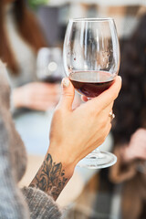 Close up woman hand with tattoos holding glasses with red wine. Young woman enjoying winter weekends.