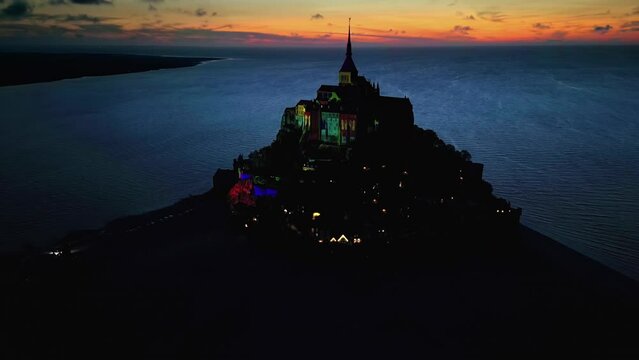 Aerial drone view of Mont-Saint-Michel at sunset in Normandy, France. Illumination in the town, water of the English Channel