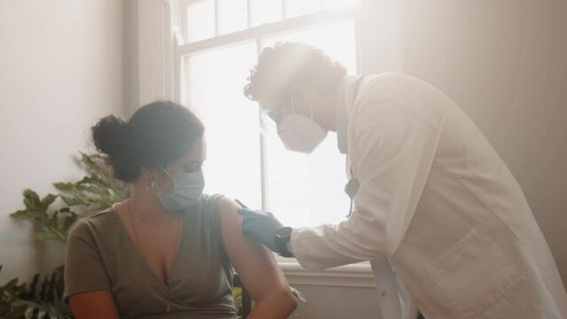 Doctor wearing a face mask inoculates a patient with the covid-19 shot. Medical professional administering a vaccine in a home visit as a way to flatten the curve of coronavirus infections.