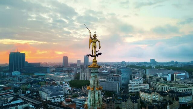 Aerial drone view of statue of Saint Michael atop the spire of the Brussels Town Hall at sunset in Belgium. Multiple buildings on the background