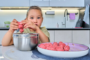 A girl is preparing meatballs in the kitchen.