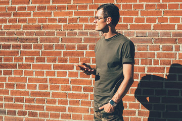 Fototapeta na wymiar pensive man in trendy apparel holding smartphone device near wall
