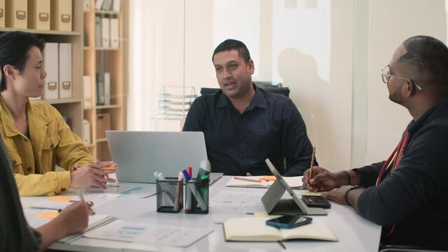 Medium shot of male director meeting his team at conference table in office and brainstorming