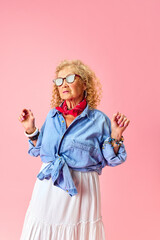 Fashionable lady. Portrait of beautiful old woman in stylish skirt and shirt standing over pink studio background. Concept of human emotions, fashion, elderly people, lifestyle, creativity. Ad