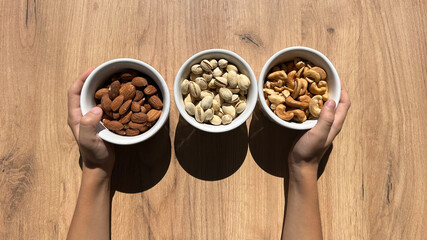 three bowls with nuts on a wooden table in children's hands.