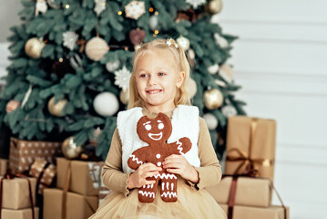 Merry Christmas and Happy Holidays. Child girl eating big iced gingerbread man cookies under Christmas tree Waiting for Christmas. Celebration New Year.