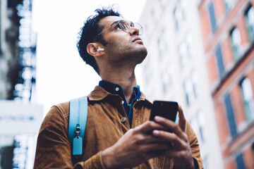 Hispanic young man in eyeglasses standing on street with smartphone