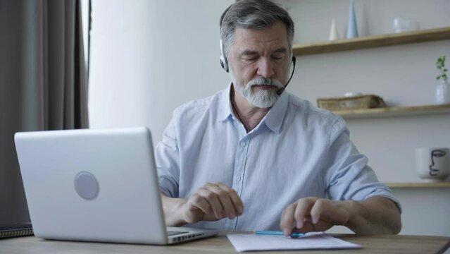 Mature businessman wear headphones making video conference business call on laptop speaking communicating by webcam, male teacher manager talking do online chat on computer sit at home office desk