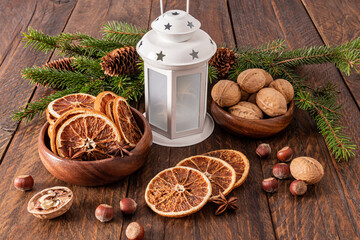 Festive Christmas arrangement with dried orange slices in wooden bowl, walnuts, white christmas lantern. Rustic style.