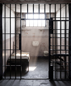 Sunlight streaming through window of empty prison cell, illuminating the bed