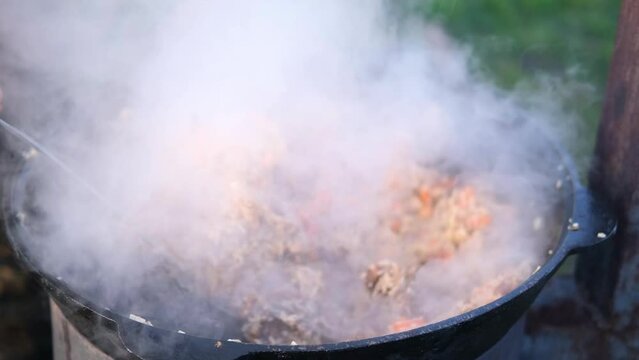 Cooking traditional pilaf in a cauldron in nature, outdoors. Eastern, oriental national Uzbek rice dish. Uzbek pilaf of beef, lamb, chicken in a large cauldron with vegetables.