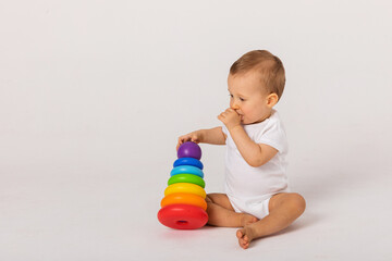 Little boy playing logic educational games with plastic pyramid isolated on white background. A happy child plays with an educational toy. The baby is one year old