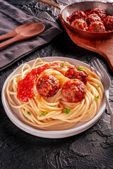 Meatballs. Beef meat balls, n a pan and with a plate of spaghetti pasta, on a black slate background