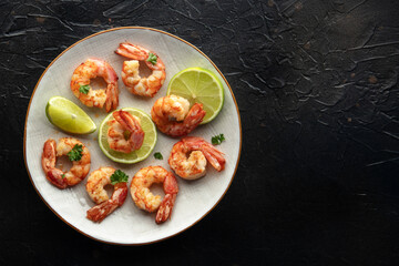 Shrimps, overhead flat lay shot with copy space. Fried shrimp with lime on a white plate, shot from the top on a black slate background. Keto appetizer