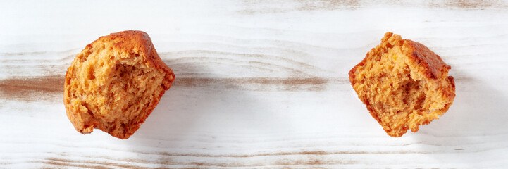 Broken orange muffin on a rustic wooden kitchen table panorama, top shot with copy space