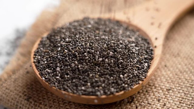 Healthy organic chia seeds falling on a kitchen wooden spoonful with rustic burlap close up. Rotation