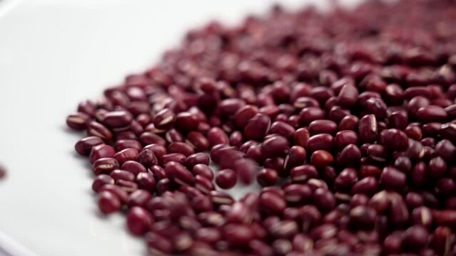 Red mung beans or adzuki grains on a white ceramic dish close up. Rotation