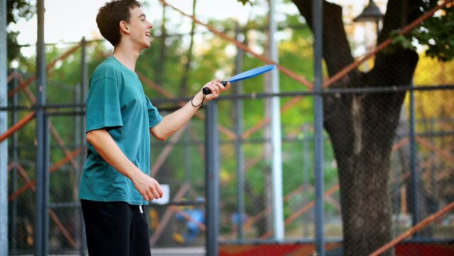 Young guy playing Pickleball, hitting the ball with a racket on an outdoor court. Slow motion