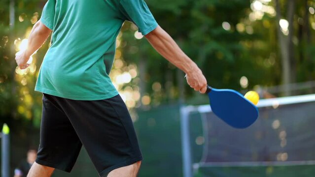 Man playing Pickleball, hitting the ball with a racket on an outdoor court. Slow motion