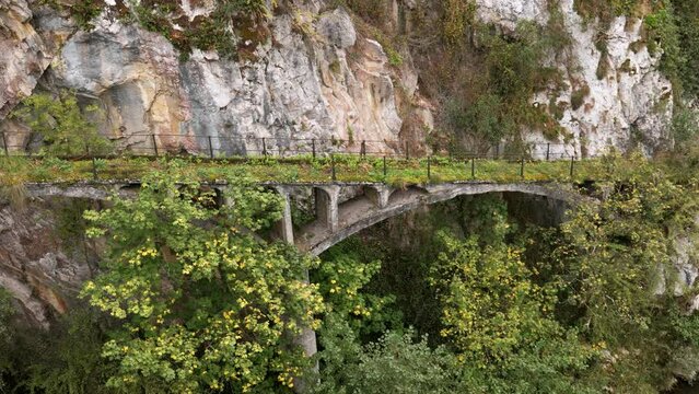 Ancient rock arched stone bridge with mountain river and autumn trees