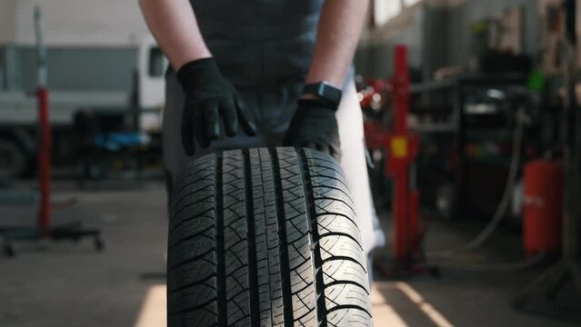 front view, the hands of a car mechanic rolling a wheel in the workshop