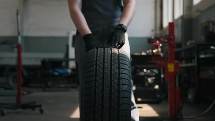 front view, the hands of a car mechanic rolling a wheel in the workshop - Powered by Adobe