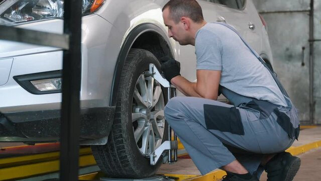 A car service employee installs a wheel adapter with a target on the wheel to perform a wheel alignment. Diagnostics and balancing.