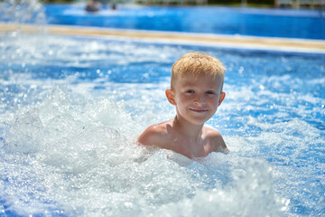 Fototapeta na wymiar Young boy kid child eight years old splashing in swimming pool having fun leisure activity. Boy happy swimming in a pool. Activities on the pool, children swimming and playing in water, happiness and