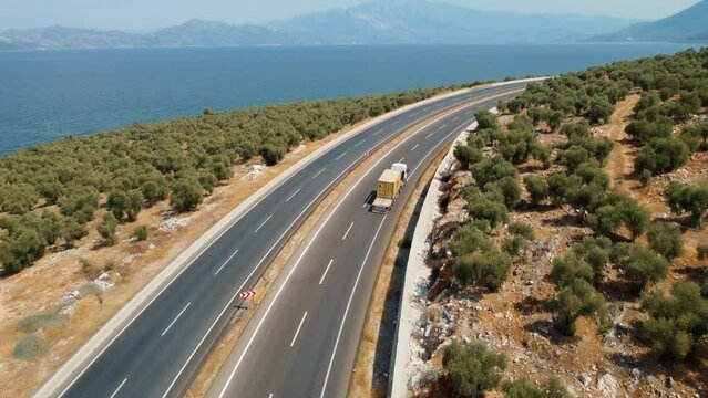 Aerial shot of heavy truck truck by cargo trailer moving through mountains on modern highway along lake or sea. Logistics Delivery Concept. car moving along highway view from drone.