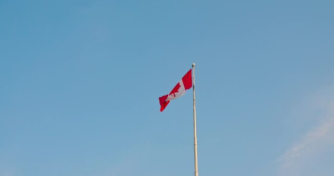Canada flag flutters high in wind far away. Slow motion video of Canadian flag on flagpole is flapping at day time. Concept maple leaf on Canadian flag is symbol of Canada's fertility. Canadian life