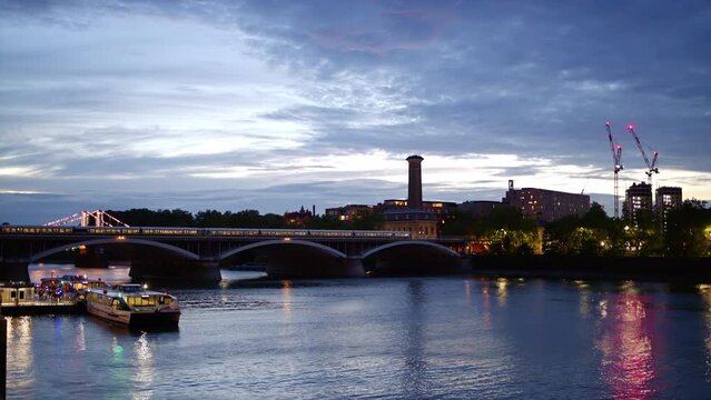 Cityscape of the London at evening, United Kingdom. Thames river, train moving on the bridge, greenery and buildings with illumination