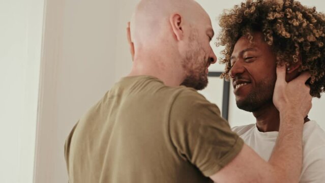Heartwarming slow-motion footage of a diverse gay couple in love, with an African curly-haired male and his Caucasian homosexual partner dancing gracefully at home
