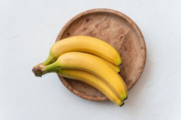 Ripe yellow fruit bananas on wooden plate. White background. Healthy tropical food. Top view