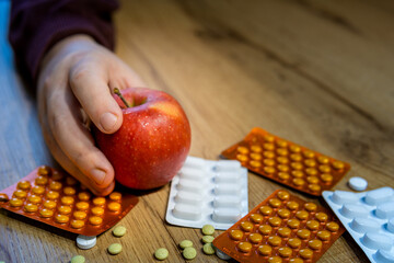 An apple a day keeps doctor away, hand holding an apple dominate over pills spread on the table