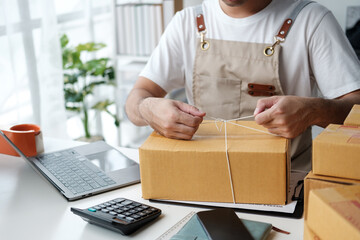 Asian man checking order and customer's details and addresses on laptop or box in order to prepare for shipping according to the information, Online shopping SME entrepreneur