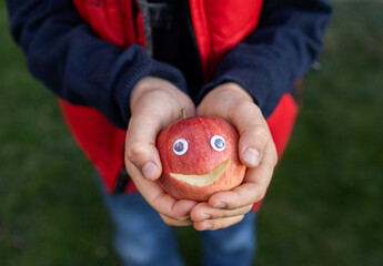 Red apple with eyes and a smile carved on it in the hands of a child. positive concept, give people...
