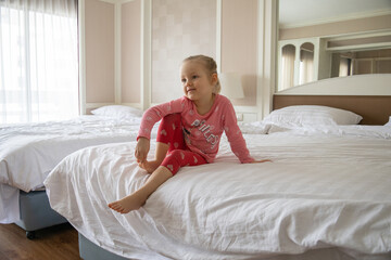 Little blonde girl with interest watches TV while sitting on a bed in a hotel.