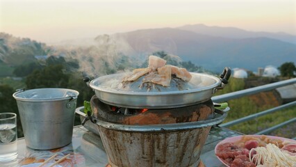 Moo Kata, Thai BBQ grill pork on circle hot pan. Popular Thai barbecue dish. Pork is grilled on pan with smoke and mountains view on background.