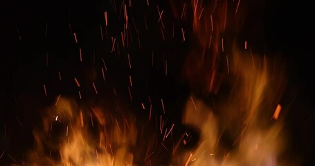 Fire and sparks at night close-up, slow motion. The flames of burning wood log fire on black background