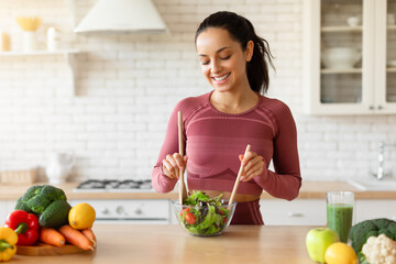 Fitness woman making fresh salad in her kitchen at home