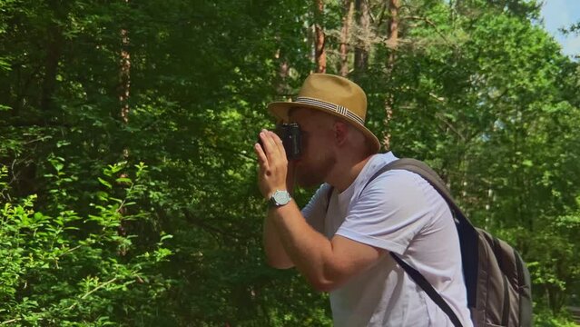 Attractive man photographer exploring national park, taking photos of trees and plants in forest.  Travel and adventure concept. Young journalist photographing nature for publication