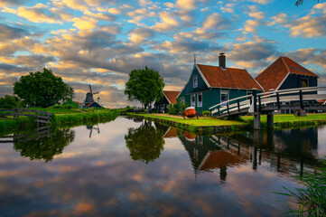 Obraz premium Colorful sunset above historic farm houses in the holland village of Zaanse Schans near Amsterdam with beautiful reflection in water.