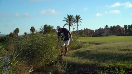 Older man looking for lost balls around a golf course lake. Sunny day at sunset - Powered by Adobe