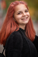 Naklejka premium Portrait of a young beautiful red-haired girl in black jeans and a black sweater in an autumn park.
