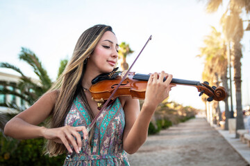 american shot of a violinist girl playing the violin a walk in the countryside in the sunset. © Boscaeta